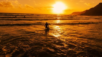Fototapeta premium Silhouette of a surfer walking into the ocean illuminated by the setting golden sun