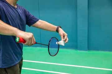 Badminton player hand serving holding shuttlecock and professional badminton racket at indoor sport badminton court