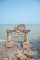 an old stone bridge over water near beach and rocks under blue sky