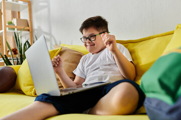 adorable boy with Down syndrome sitting on yellow couch, using laptop.