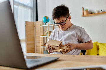 A boy with Down syndrome sits diligently at a desk, focusing on his laptop.