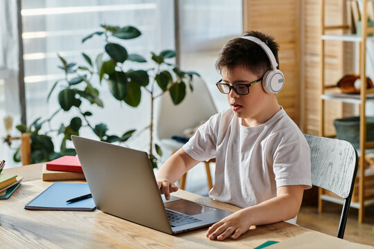 A boy with Down syndrome uses a laptop at home while wearing headphones.