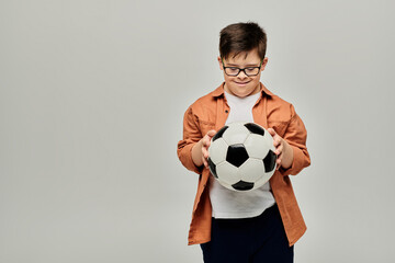 A boy with Down syndrome with glasses holds a soccer ball