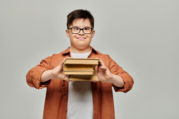 A boy with Down syndrome happily holds a stack of books on a gray background.