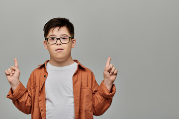 A little boy with Down syndrome with glasses playfully gesturing with his finger.