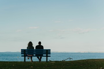Couple sits on a bench overlooking a stunning beach