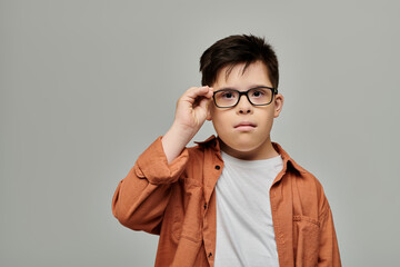 A charming boy with Down syndrome with glasses strikes a pose against a gray backdrop. © Bliss