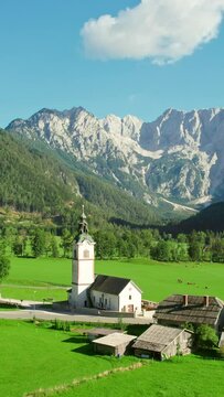 Traditional Slovenian Church of St. Andrei in Ravenska Kocna valley with the Kamnik-Savinja Alps in the background. An aerial summer view of the idyllic Alpine landscape in Zgornje Jezersko, Slovenia