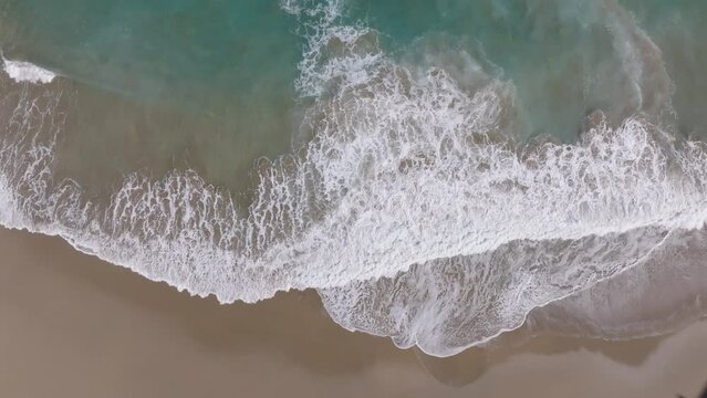 Plano cenital grabado con Drone de unas preciosas olas de agua azul llegando a la orilla cubriendo la dorada arena de la playa de Getaria en Gipuzkoa (Pa&iacute;s Vasco).
