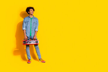 Full size portrait of nice young man boombox look empty space wear denim shirt isolated on yellow...