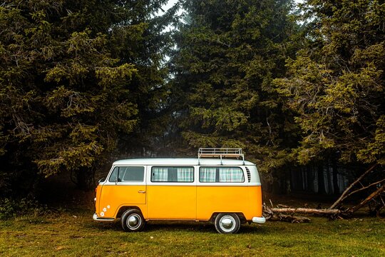 Orange vintage van driving through the forests of Parc du Pilat in France in autumn.
