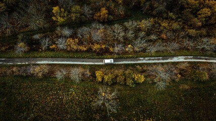 Aerial shot of a vintage van driving through the forests of Parc du Pilat in France in autumn.