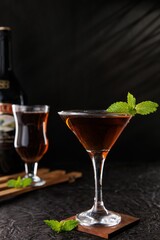 Glass of cocktail garnished with mint leaves in a dark room