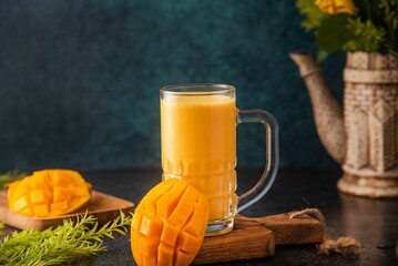 Glass of creamy mango smoothie atop a small wooden cutting board with slices of mango