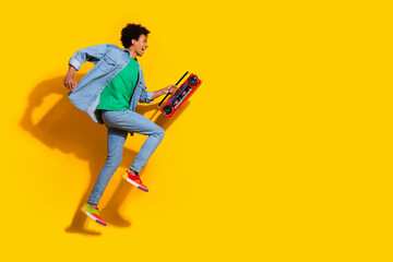 Full size portrait of nice young man boombox jump run empty space wear denim shirt isolated on yellow color background