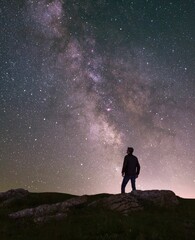 Fototapeta premium Mature man stands on a hilltop, with a magical star-filled night sky visible in the background