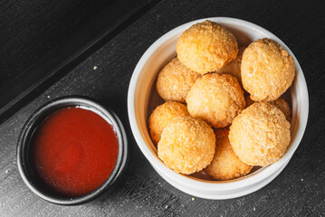 Golden-brown breaded balls, possibly cheese or meatballs, served with red sauce in a black dish