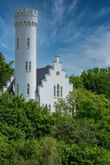 Majestic white tower standing tall against a backdrop of lush green trees and a bright blue sky