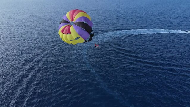 Two People Parasailing over Sky Blue Sea on Double Canopy Tugged by Boat, Drone Back View