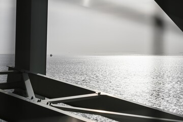 Grayscale of a detail of a metallic bridge above the sea on a sunny day