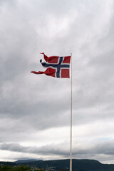 The flag of Norway flowing in the wind with clouds in the background.