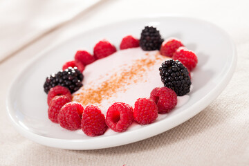 Raspberries and blackberries laid out on a white plate in circle with yogurt and cinnamon