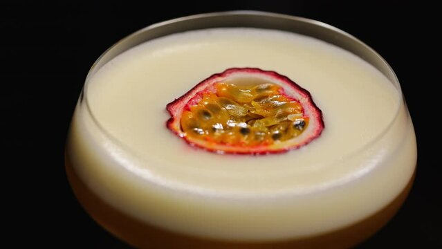 Half of exotic passion fruit decorating classically performed porn star martini cocktail with creamy consistence. Alcoholic beverage with sour refreshing taste isolated on black background.