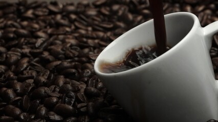 Fresh espresso was poured in white cup with pile of coffee bean. Pouring black coffee in the cup...