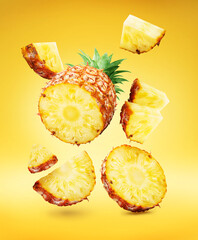 Pineapple slices and pineapple pieces levitating in air on yellow background. File contains...