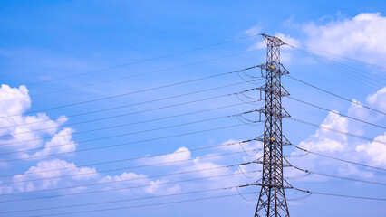 High voltage transmission tower with many cable lines against white clouds on blue sky background