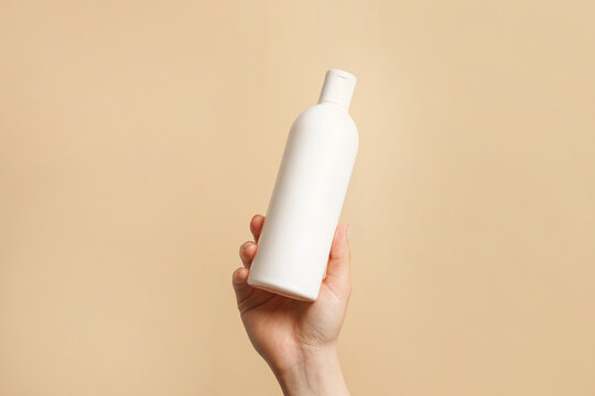 Hand holding white bottle of shampoo or hair conditioner on beige background, copy space