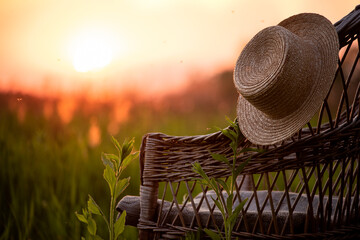 straw hat on an old wicker chair in a field overlooking the sunset on a summer evening.