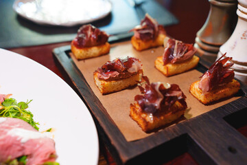 Toast with jerky on a wooden tray. Delicious snacks and original serving of dishes in the restaurant. Catering for the party.