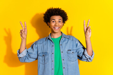 Photo of nice young man show v-sign wear denim shirt isolated on yellow color background