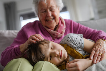 Sleeping girl lying head on gradmother knees. Portrait of an elderly woman spending time with...