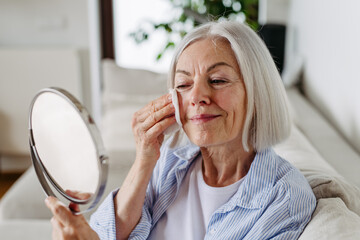 Skincare for mature woman. Portrait of beautiful older woman with gray hair cleaning, taking care of her skin.