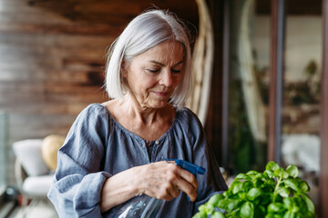 Portrait of beautiful mature woman taking care of plants on balcony. Spending free weekend at home.