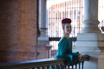 Young, pretty, blonde woman in typical green colored flamenco suit, posing leaning on a wrought iron railing. Flamenco concept, typical Spanish, Seville, Andalusia.
