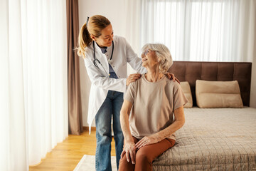 Family doctor comforting senior woman on a bed during her home visit.