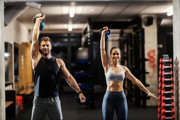 Portrait of a happy sportspeople standing in a gym and lifting kettlebells.