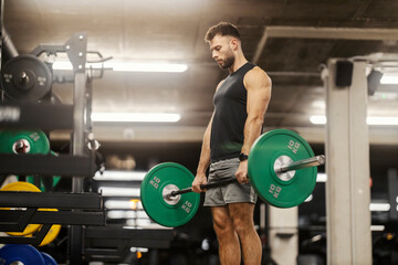 A strong muscular sportsman is doing deadlifts in a gym.