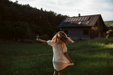 Little girl in front of house with solar panels on roof, jumping, dancing and having fun. Concept...