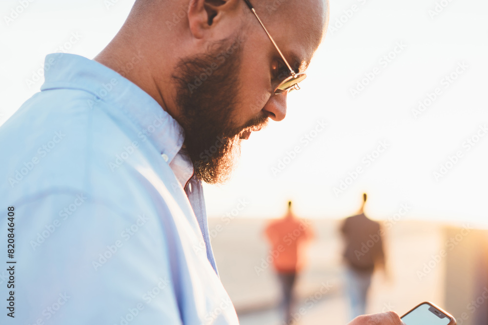 Poster young handsome guy holding smartphone making transaction via banking application standing on street,