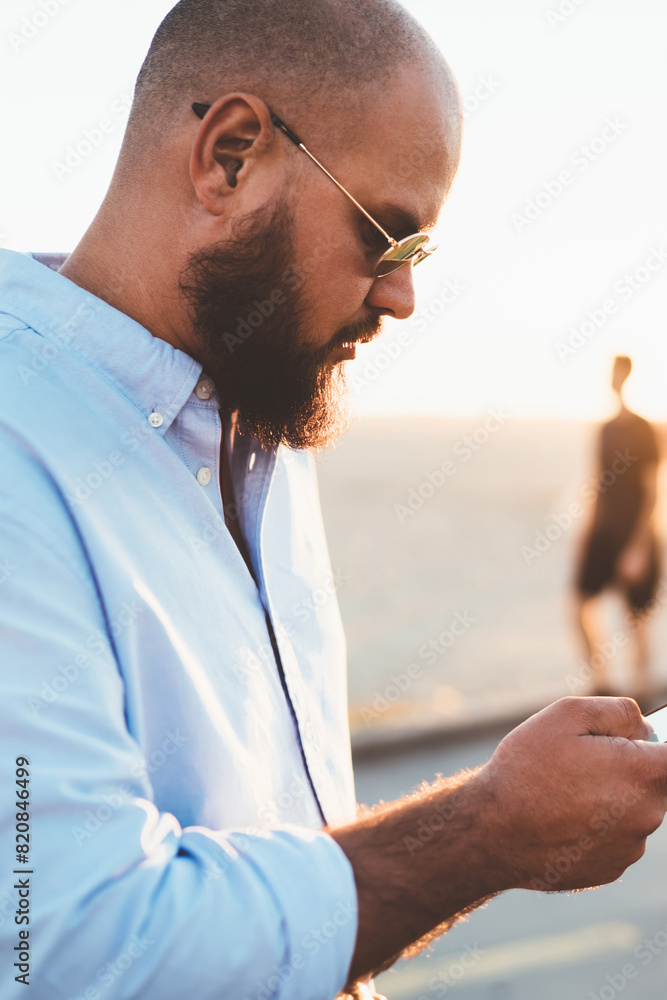 Poster pensive bearded guy installing application on smartphone via good internet connection on street, mal