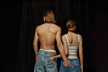 Young people, man and woman wearing jeans, posing against black studio background. Male and female...