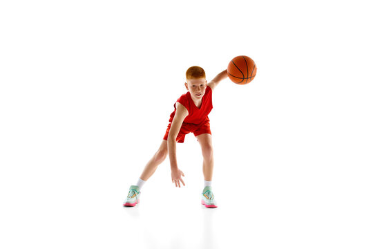 Motivated teen boy, basketball player in dynamic pose with ball, practicing, playing isolated on white studio background. Concept of sport, childhood, sport school, active lifestyle