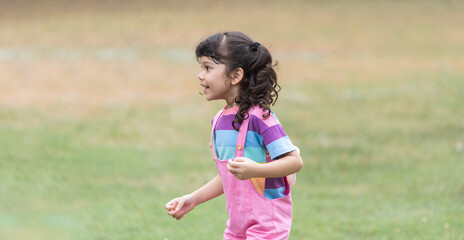 Portrait of Caucasian child girl in park playing outdoor in nature. Little girl standing, laughing, smiling in casual clothes. Education, healthy activities. Side view