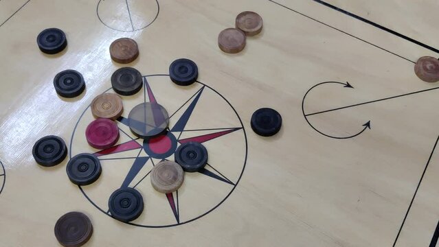 Footage of a carrom board with carrom coins on the board hit with a striker kept at one end of the board