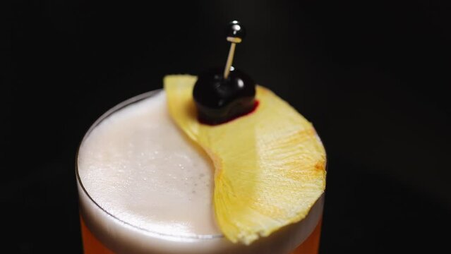 Details of amaretto sour cocktail decorations in form of dried pineapple slice pierced with metal skewer with black olive. Boozy refreshing drink with additional elements on top for flavour shading.