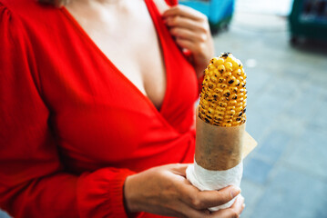 Woman in a red dress holds fried corn. Street snack.